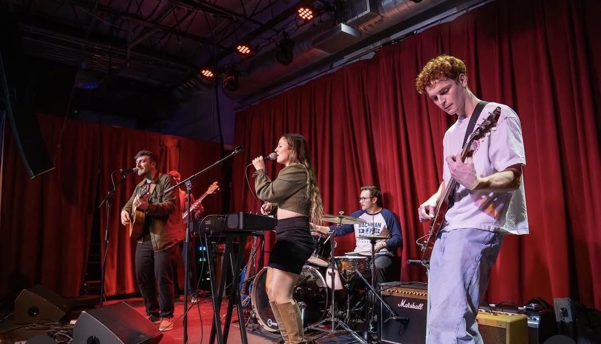 Bella performing with a full band on a stage with red curtains