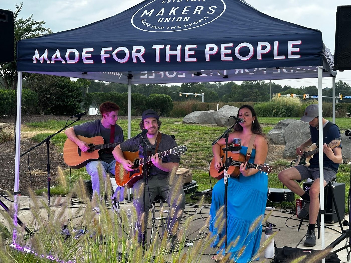 Bella performing with a band outdoors under a 'Made for the People' tent