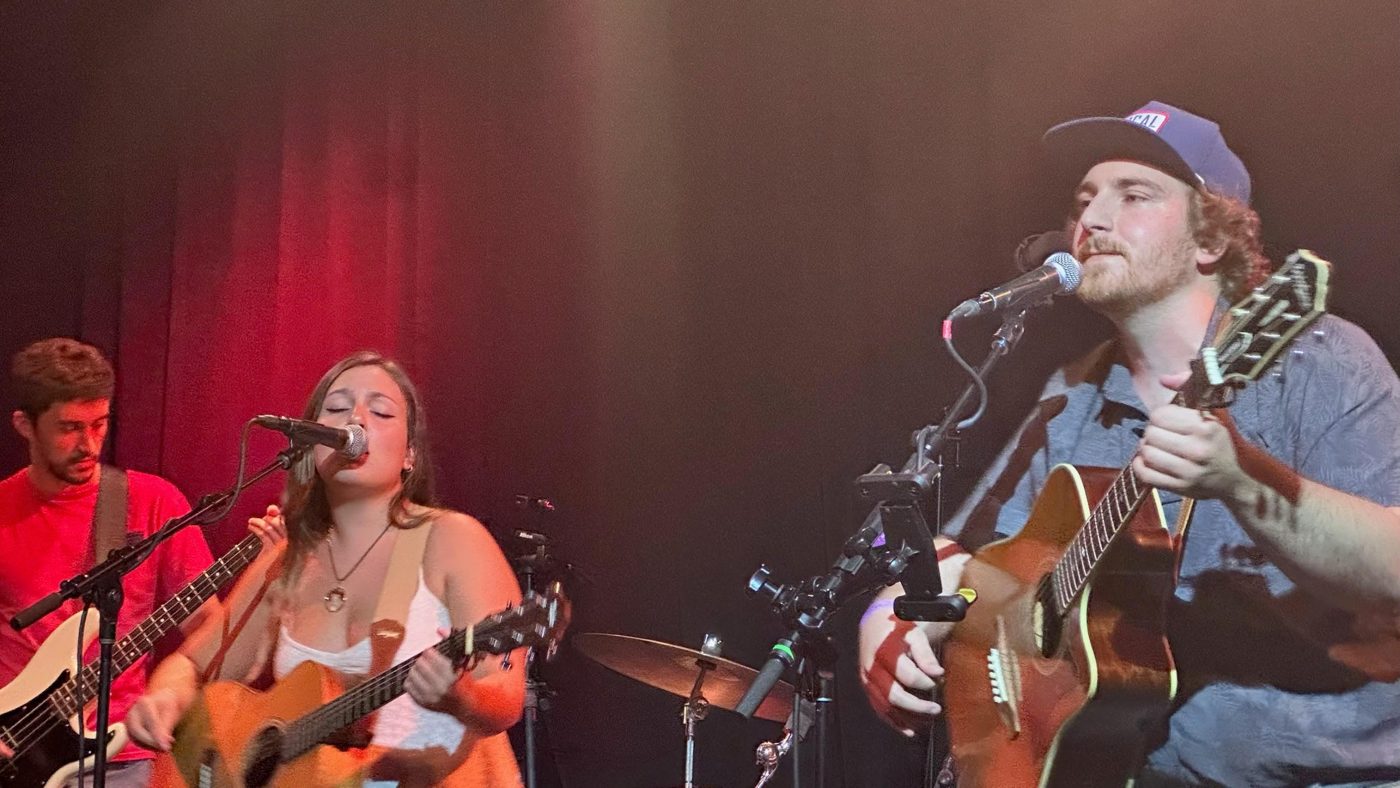 Bella performing with guitarists on a red-lit stage