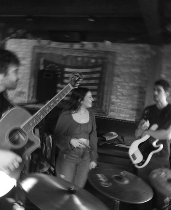 Black-and-white photo of Bella smiling onstage between a guitarist and a bassist