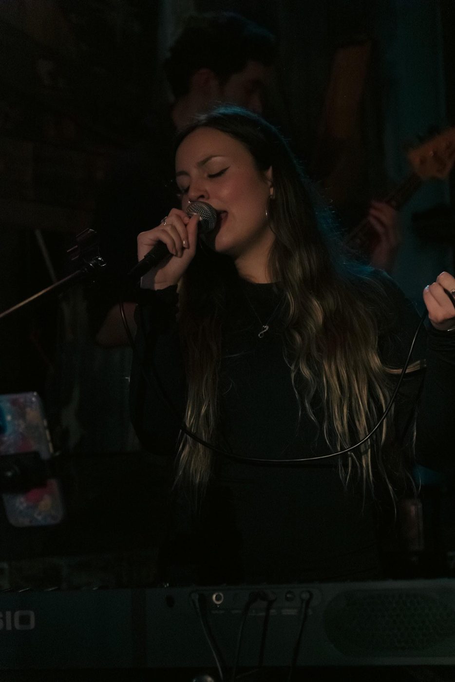 Bella singing into a microphone in low stage light