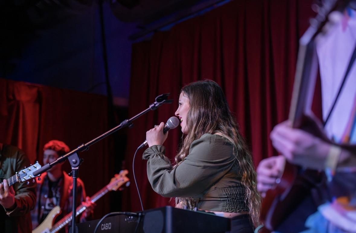 Bella singing on a red-lit stage with a band