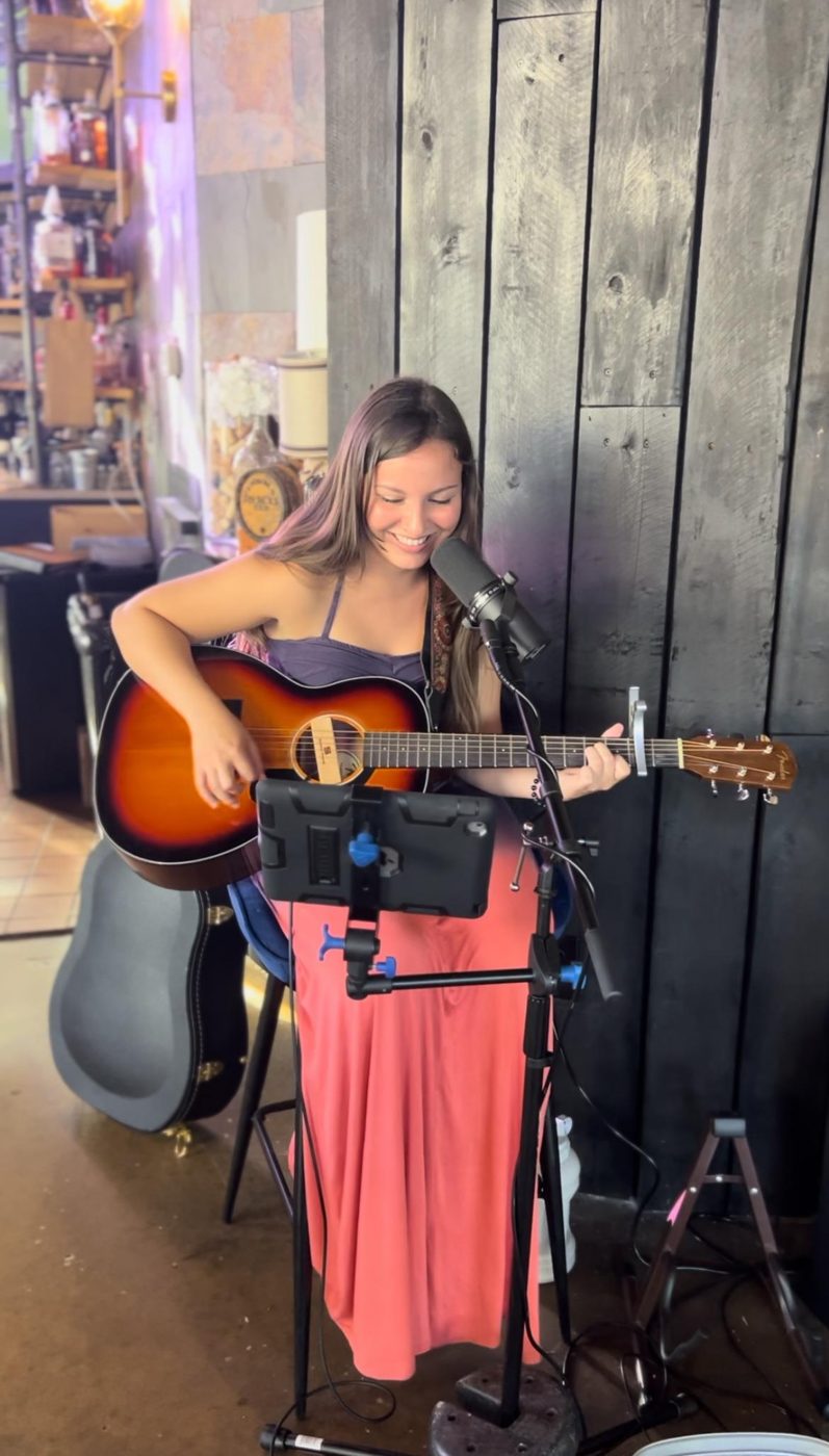 Bella singing and playing acoustic guitar at a microphone